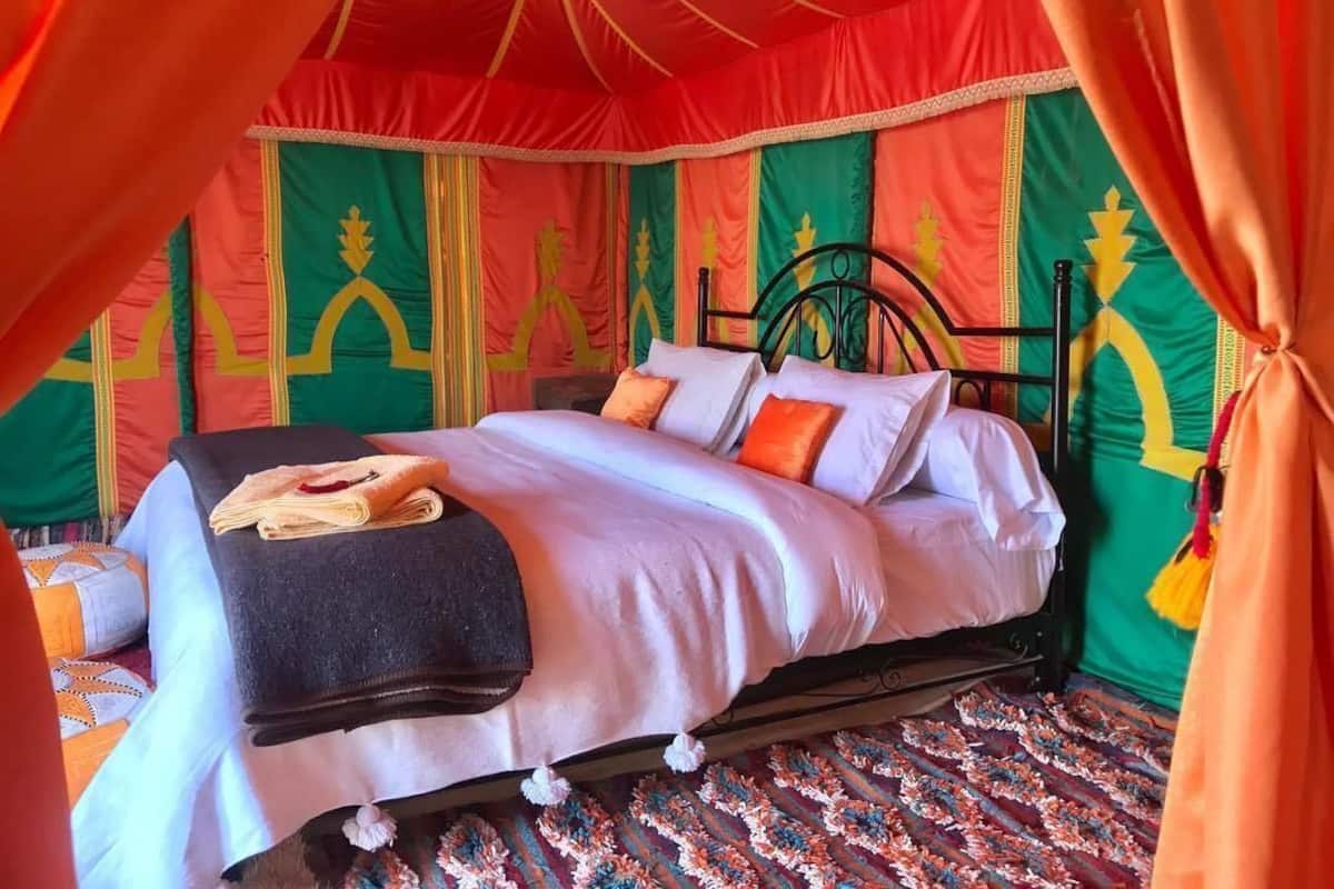 Una cama con estructura metálica negra, ropa de cama blanca y almohadas anaranjadas.