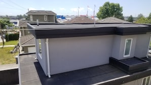Un edificio de varios pisos con techo plano, un balcón en el nivel superior y un pequeño espacio exterior con sillas.
