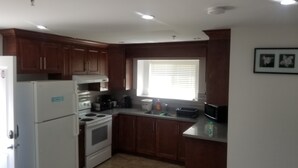 Una cocina con armarios de madera, un refrigerador, estufa y una ventana con persianas.