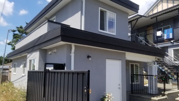 Un edificio residencial moderno de dos pisos con techo plano, un balcón en el nivel superior y una entrada con portón.