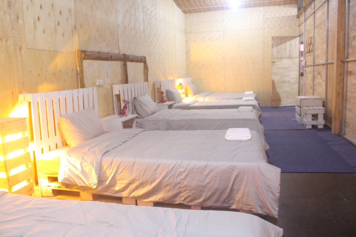A room with four single beds, wooden headboards, and bedside tables with lamps.