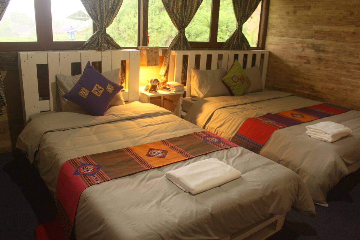A room with two beds, a nightstand, and a window with curtains.