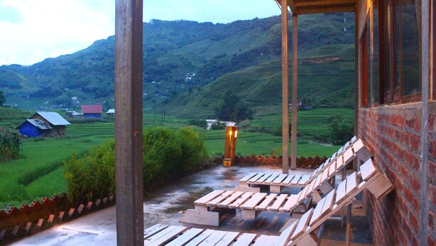 Una terraza de madera con sillones de descanso con vistas a un valle verde exuberante y casas al fondo.