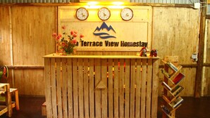Un mostrador de recepción de madera con un letrero que dice "Terrace View Homestay" y tres relojes encima.