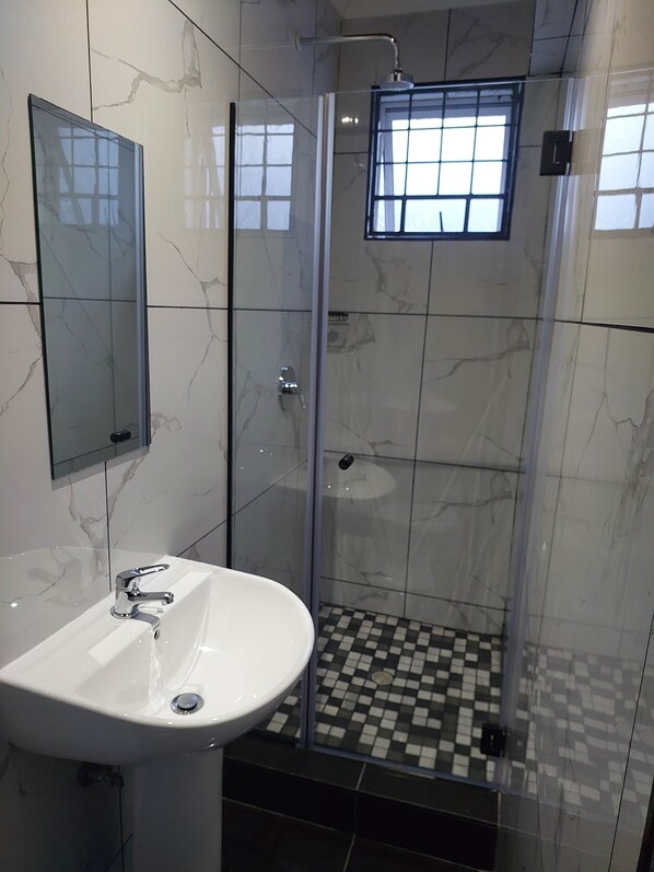 Un baño moderno con ducha de vidrio, un lavabo blanco y un espejo.