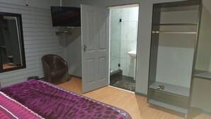A bedroom with a bed, a chair, a wardrobe, a television, and a bathroom visible through an open door. - Freedom Media Guest House (Gqeberha (Port Elizabeth))