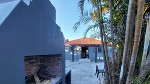 A building with a brick fireplace, a tiled patio, and a palm tree. - Freedom Media Guest House (Gqeberha (Port Elizabeth))