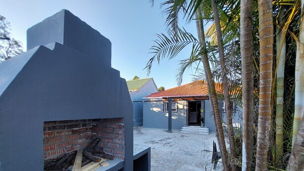 A modern outdoor barbecue area with a brick fireplace, a covered seating area, and a red-tiled roof. - Freedom Media Guest House (Gqeberha (Port Elizabeth))