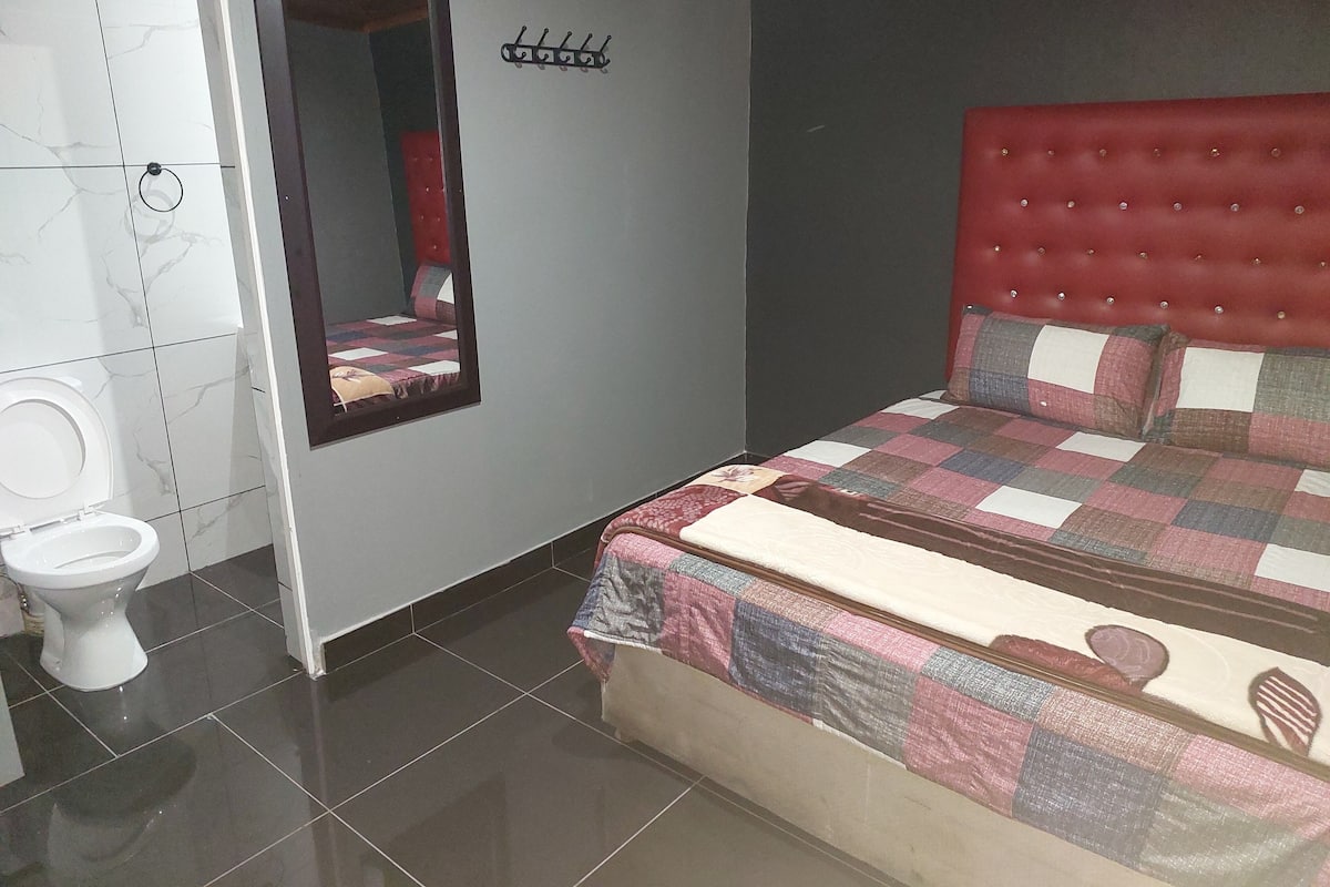 Un dormitorio con un cabecero tapizado rojo, una colcha acolchada y un espejo en la pared.