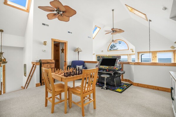 A spacious room with a wooden table set for chess, a gaming console, and a large window with a view.