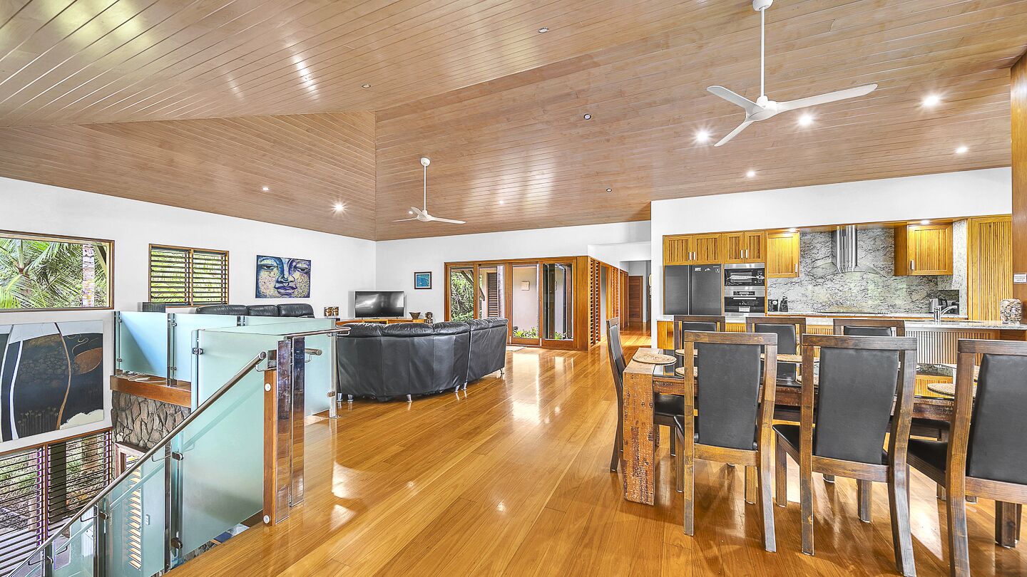 A spacious living area with a wooden ceiling, a dining area with wooden chairs, and a kitchen with stone countertops.