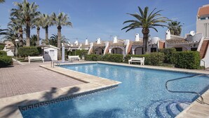 A swimming pool with a tiled edge, surrounded by palm trees and buildings with white and red roofs. - Beautiful private villa for 4 people with WIFI, A/C, pool, TV and patio (Denia)