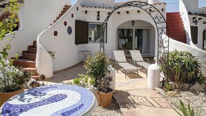 A white building with a curved staircase, a tiled patio with lounge chairs, and a mosaic fountain. - Beautiful private villa for 4 people with WIFI, A/C, pool, TV and patio (Denia)