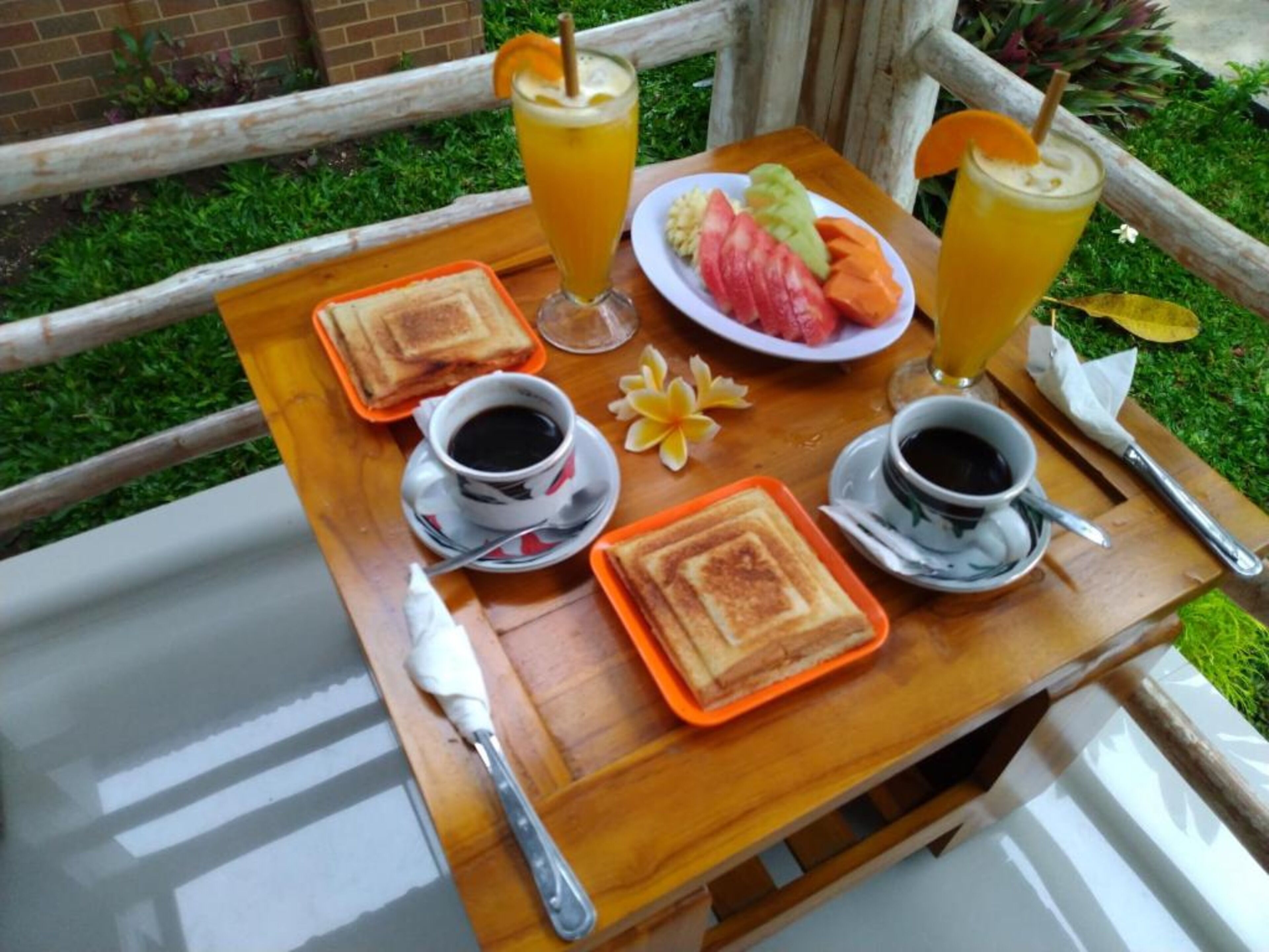 En morgenmadsopstilling med ristet brød, frugt og to kopper kaffe på et træbord.