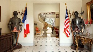 A grand hallway with two knight statues, one with a French flag and one with an American flag, leading to a staircase.