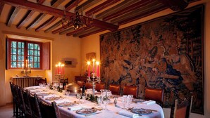 A dining room with a long table set for a meal, a chandelier, and a large tapestry on the wall.