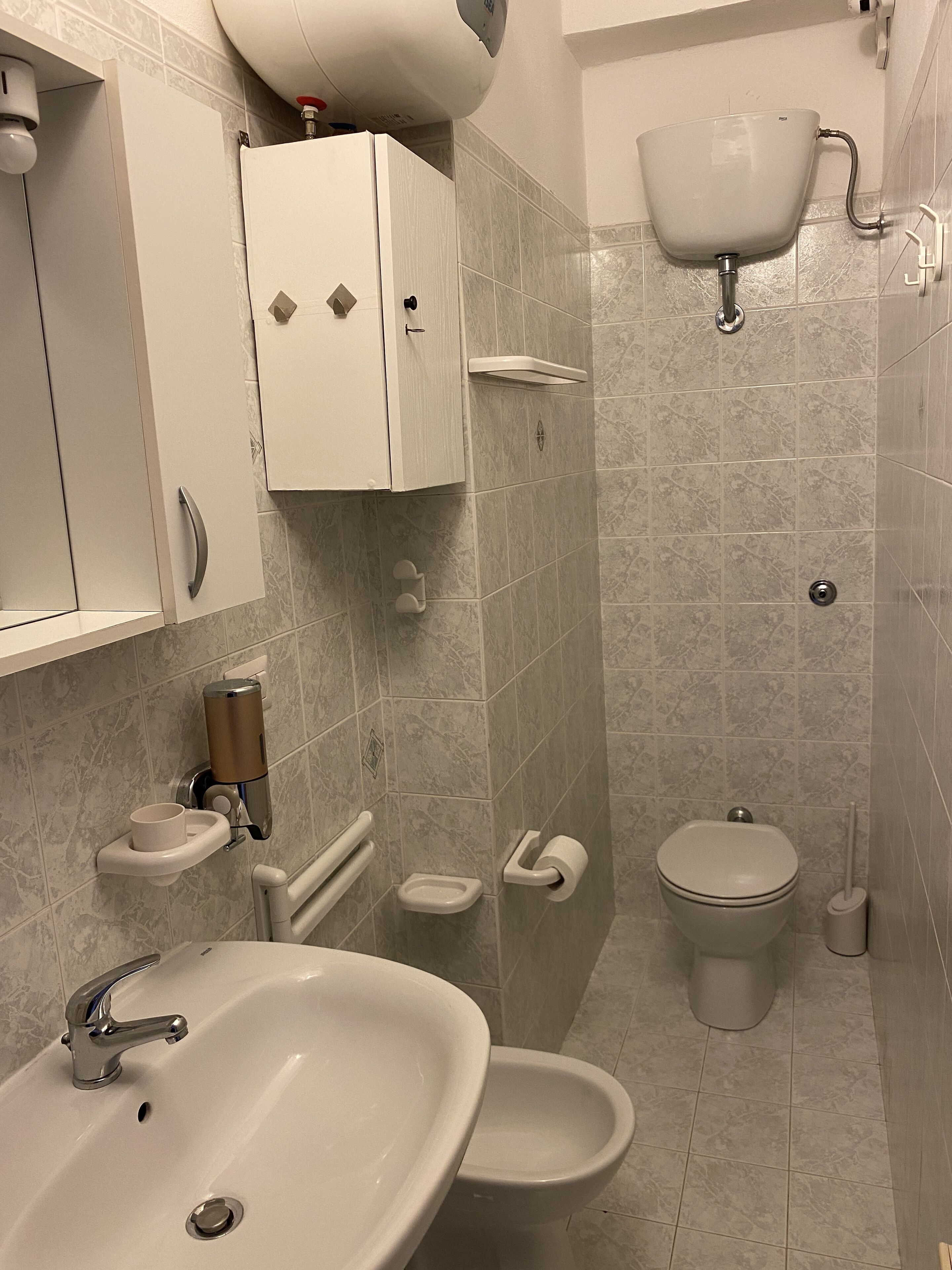 A bathroom with a sink, bidet, toilet, and storage cabinets.