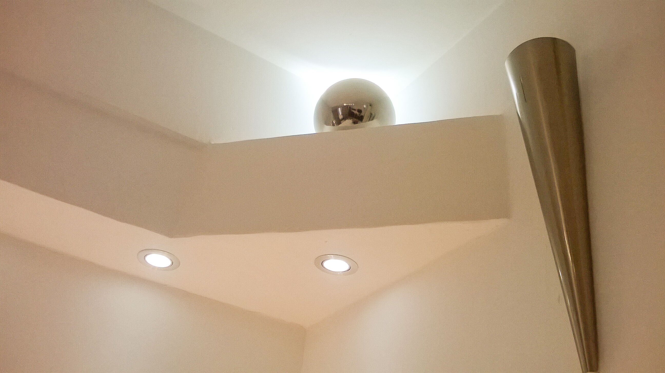 Una esquina de una habitación con techo blanco, una lámpara y un objeto metálico apoyado en la pared.