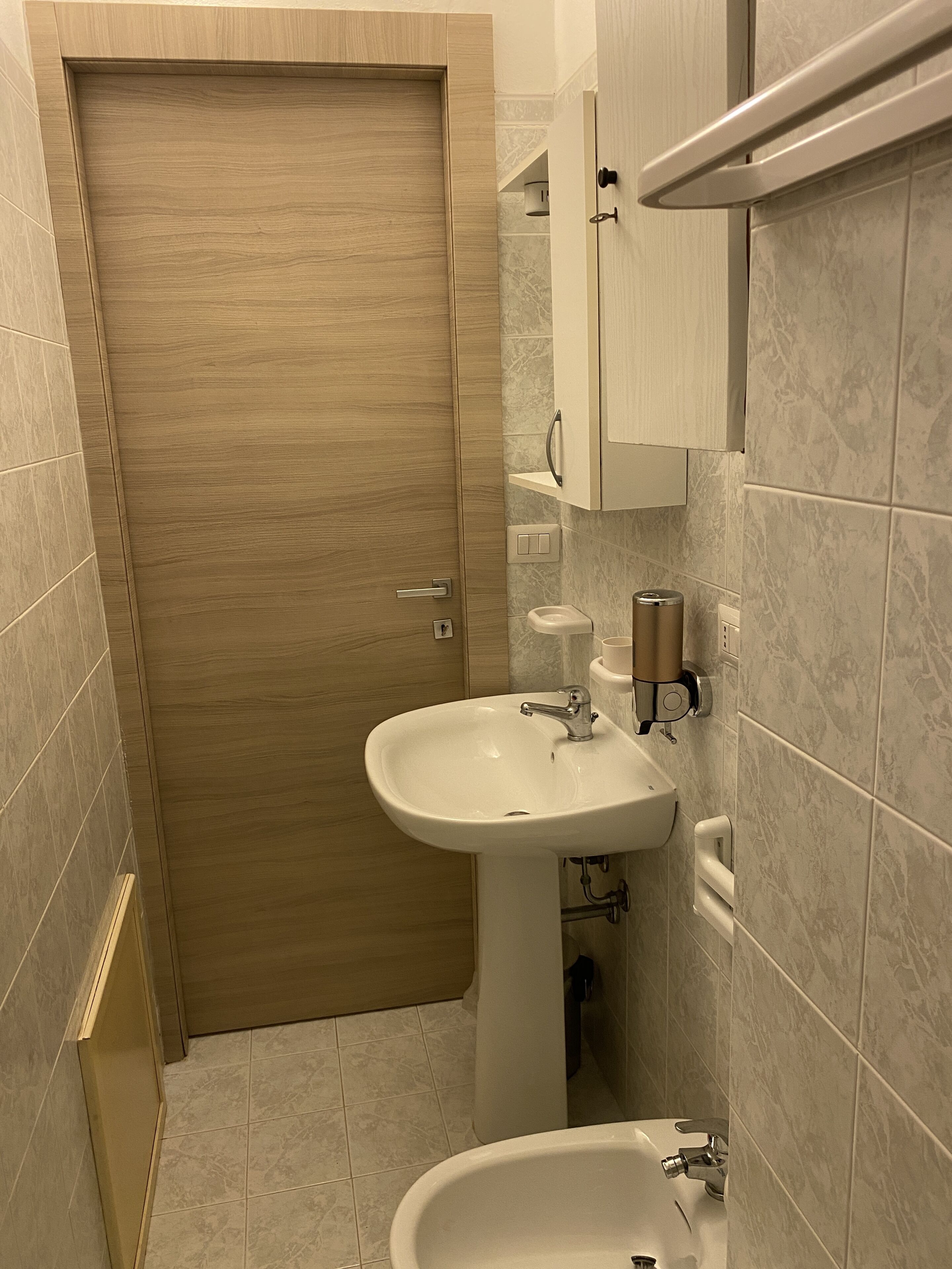 Une salle de bain avec une porte en bois, un lavabo sur colonne, un bidet et un porte-serviettes.