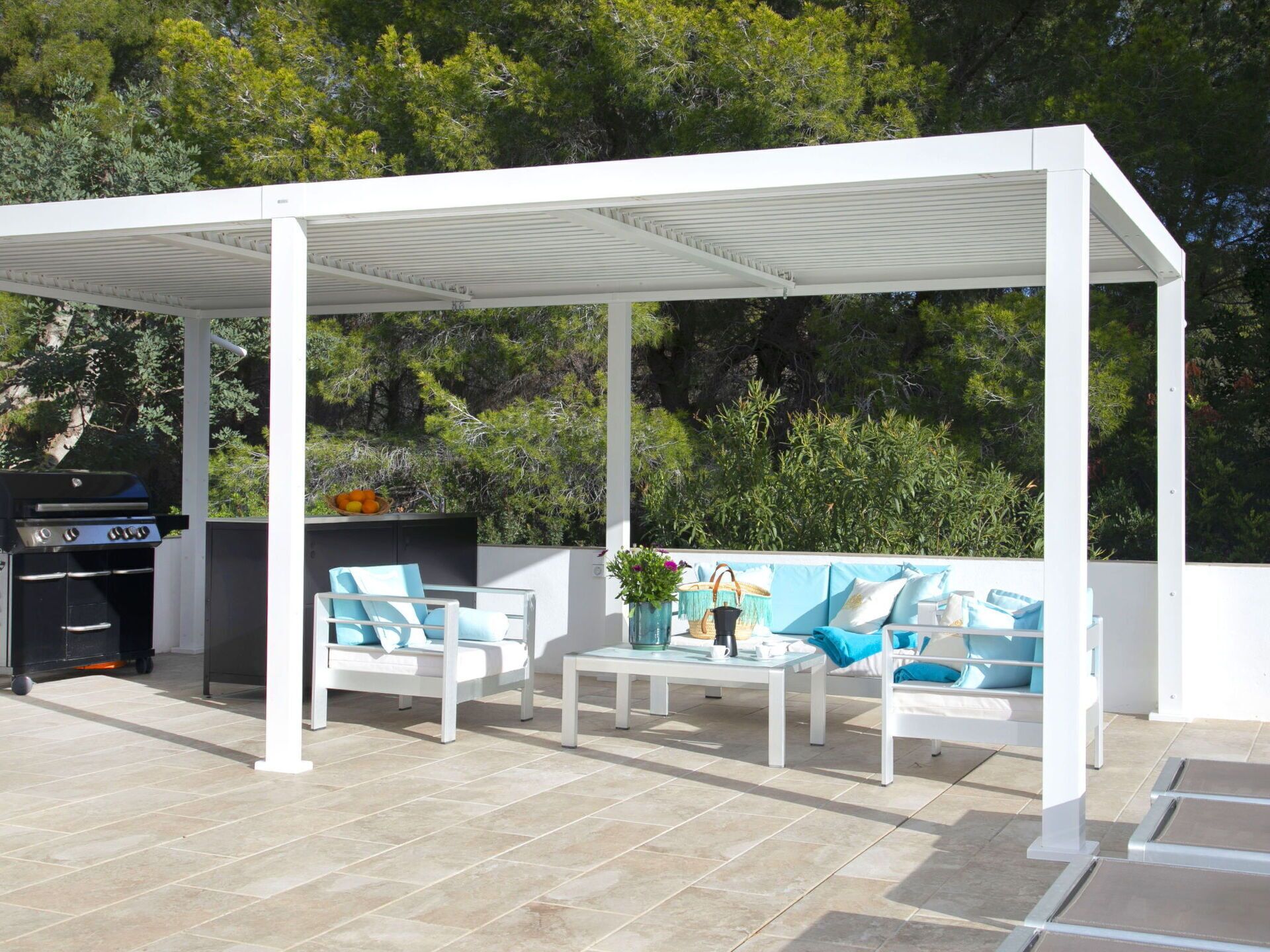 A covered outdoor seating area with a grill, white furniture, and a tiled floor.