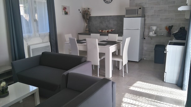 A modern living room with a sofa and a dining area with a table and chairs. There is a kitchen area with a microwave and a refrigerator. - RENTAL DOMAINE DE LA BAUME - "LE MOULIN" (Cendras)