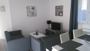 A modern living room with grey sofas, a flat-screen TV, a small table with a lamp, and decorative wall art. - RENTAL DOMAINE DE LA BAUME - "LE MOULIN" (Cendras)