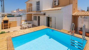 A two-story house with a swimming pool, outdoor furniture, and a barbecue area.