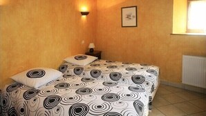 A bedroom with two beds, a wall-mounted light, a framed picture, and a window.