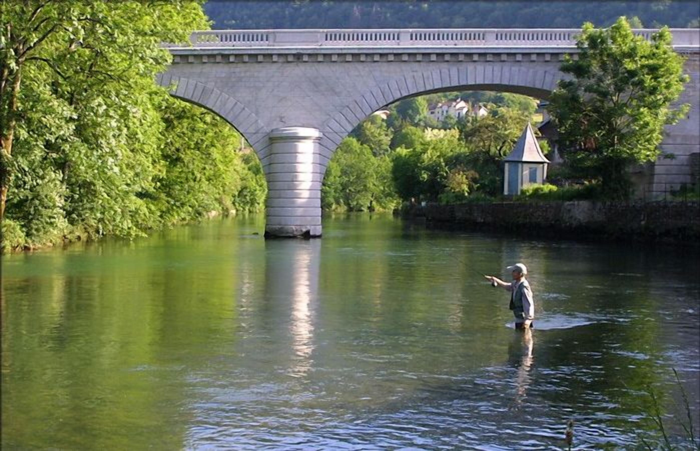 Un puente de piedra sobre un río con una persona de pie en el agua.