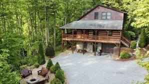 A cabin with a deck, surrounded by dense forest. - Luxury Cabin with Mountain Views, Fire pit, Hot tub and more ! (Boone)