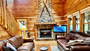 A cozy living room with leather sofas, a stone fireplace, a television, and wooden walls. - Luxury Cabin with Mountain Views, Fire pit, Hot tub and more ! (Boone)