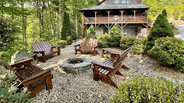 A cabin with a deck, surrounded by a gravel patio with wooden chairs and a fire pit. - Luxury Cabin with Mountain Views, Fire pit, Hot tub and more ! (Boone)