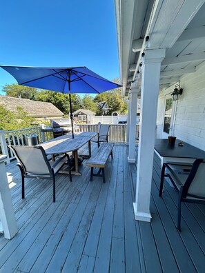 A covered outdoor patio with a table and chairs, a grill, and a blue umbrella. - Historic Edgartown House (Edgartown)