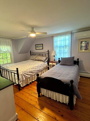 A bedroom with two single beds, a ceiling fan, a nightstand with a lamp, and a window with curtains. - Historic Edgartown House (Edgartown)