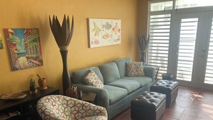 A living room with a sofa, a patterned armchair, a coffee table, and a side table with a plant and a decorative item.