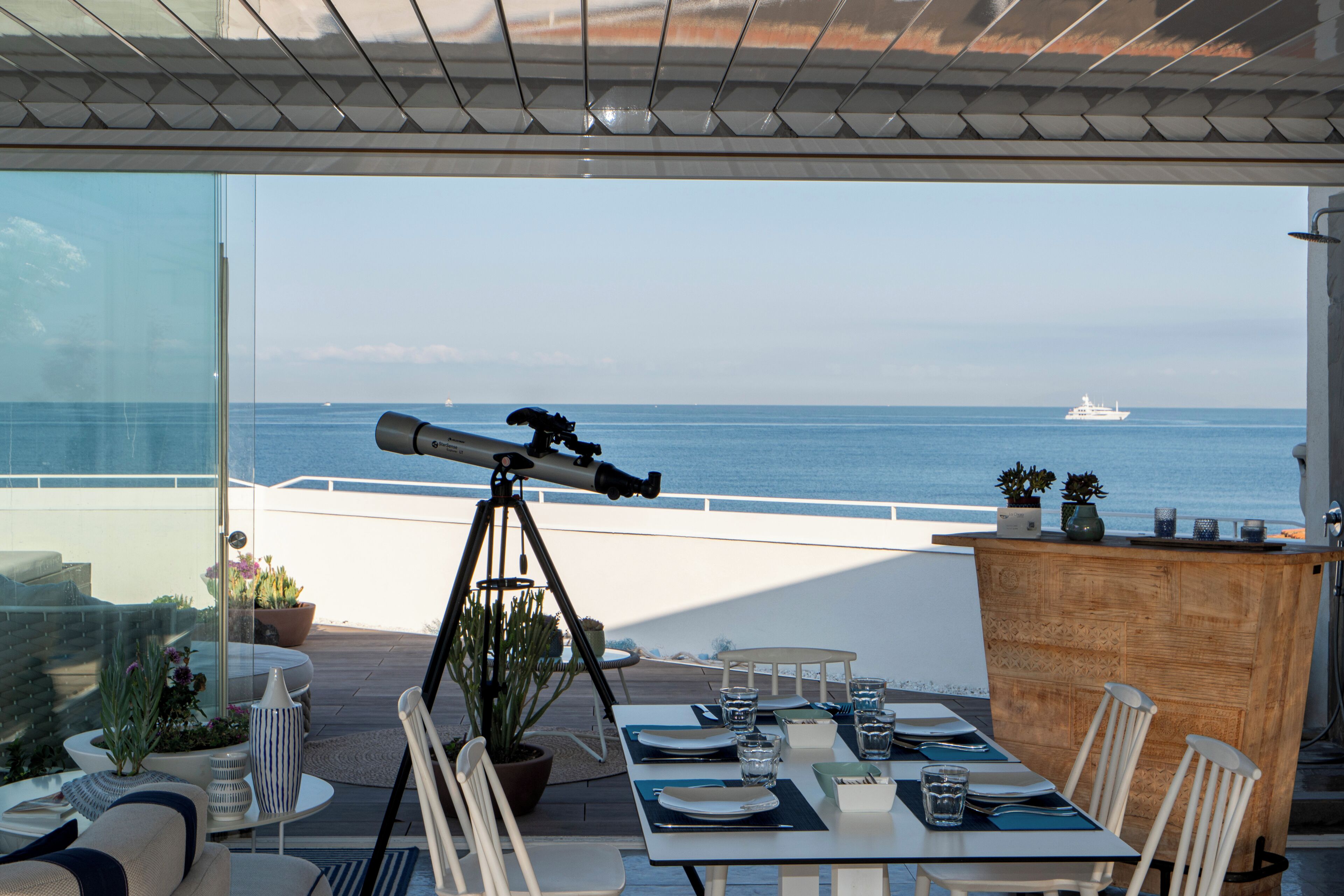 A dining area with a telescope, a table set for two, and a view of the sea.