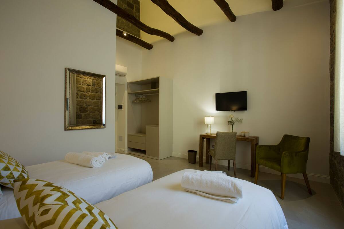 Una habitación de hotel con dos camas, un escritorio con silla, un televisor y un armario.
