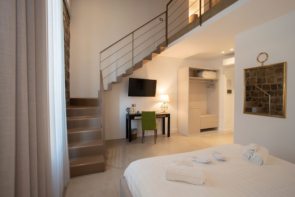 A hotel room with a bed, a desk, a chair, a TV, a staircase, and a bathroom. - La Chiaja art&relais (Castellammare di Stabia)
