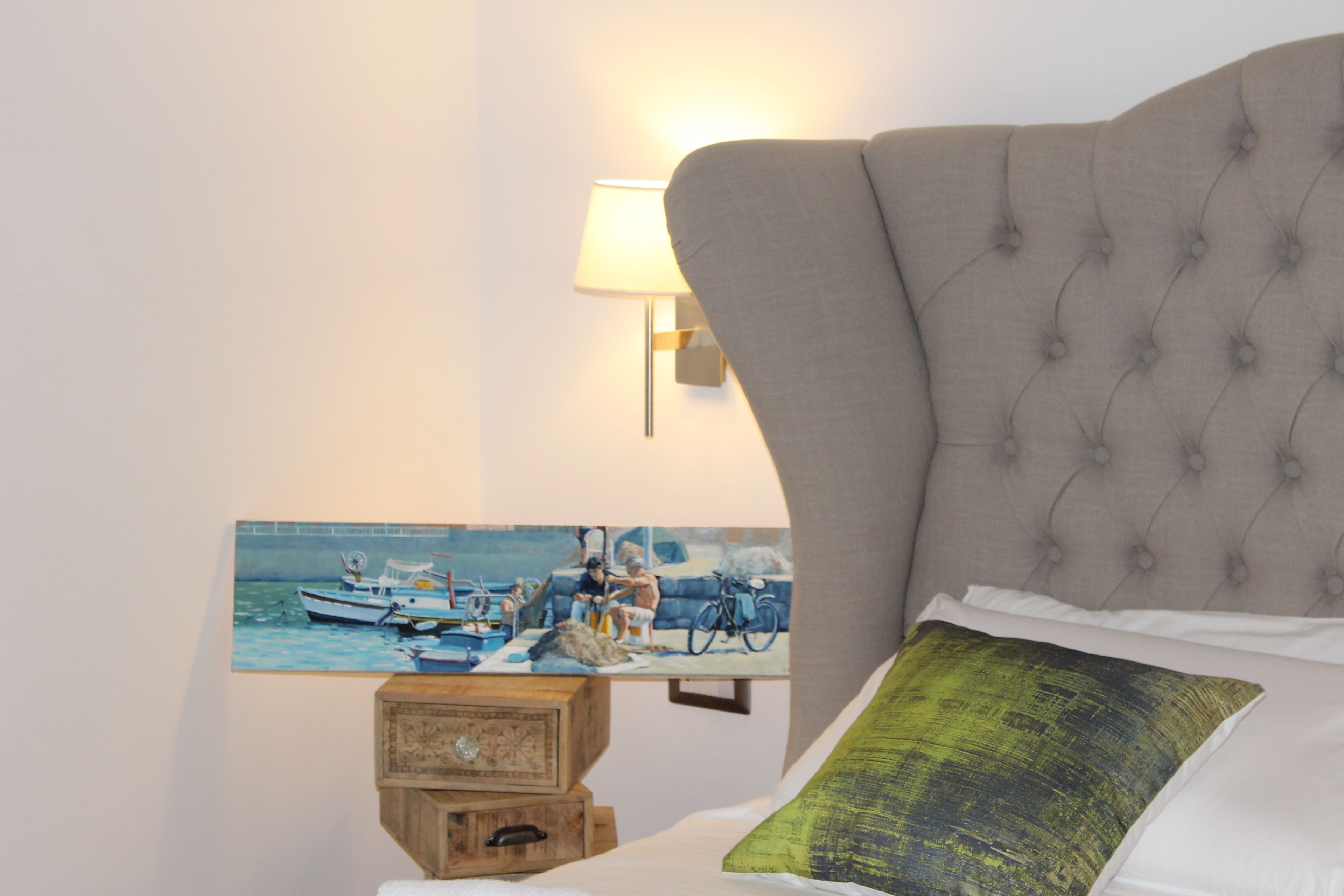 Una camera da letto con un letto, un quadro con delle barche al muro, una lampada e un baule di legno.