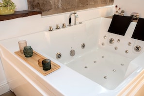 A modern bathroom with a large bathtub, a wooden tray with candles, and a decorative plant on the shelf. - La Chiaja art&relais (Castellammare di Stabia)