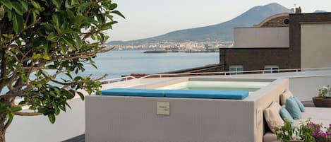 A rooftop terrace with a hot tub, seating area, and a view of the city and mountains.