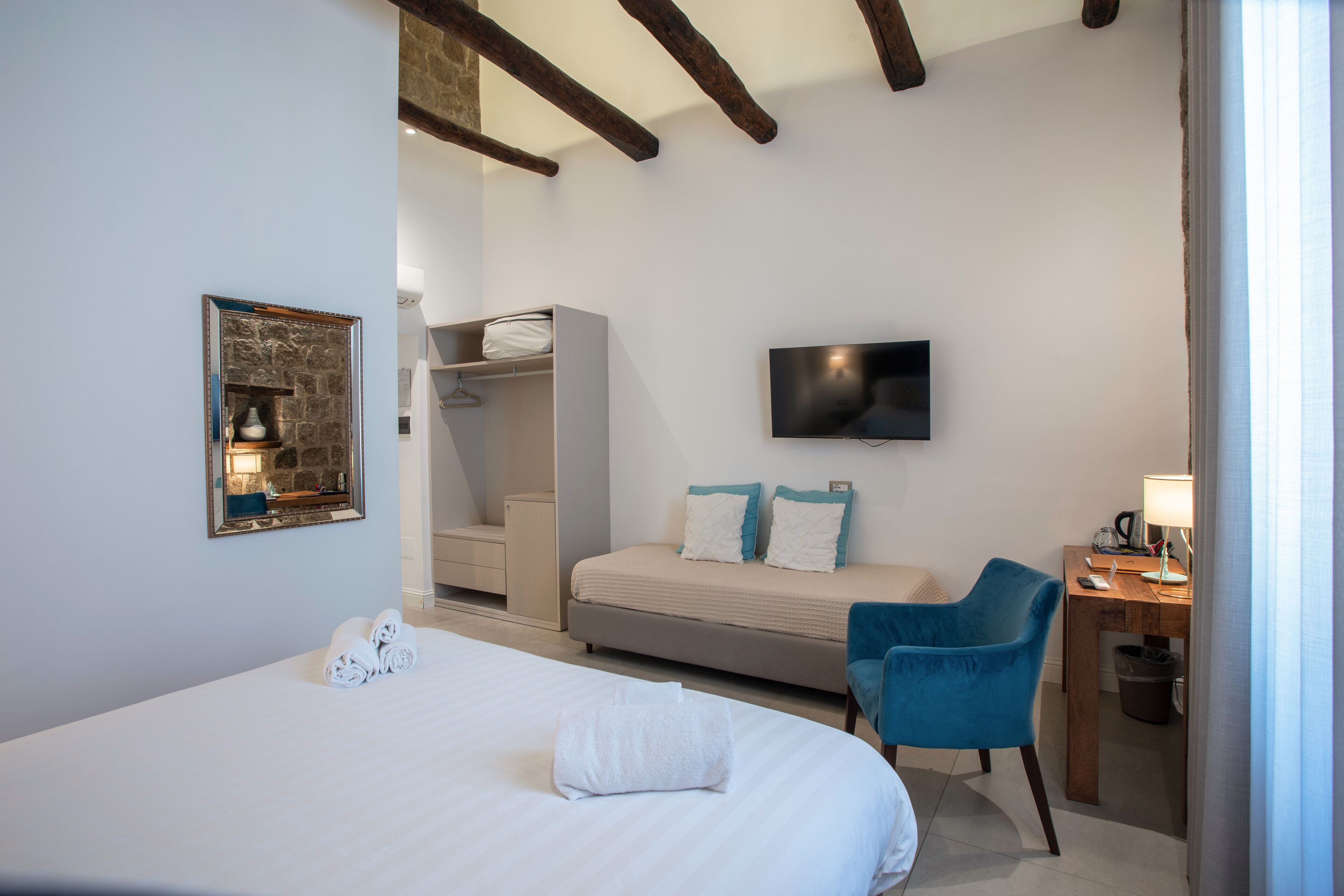 A hotel room with a bed, a desk with a lamp, a TV, a wardrobe, and a chair.
