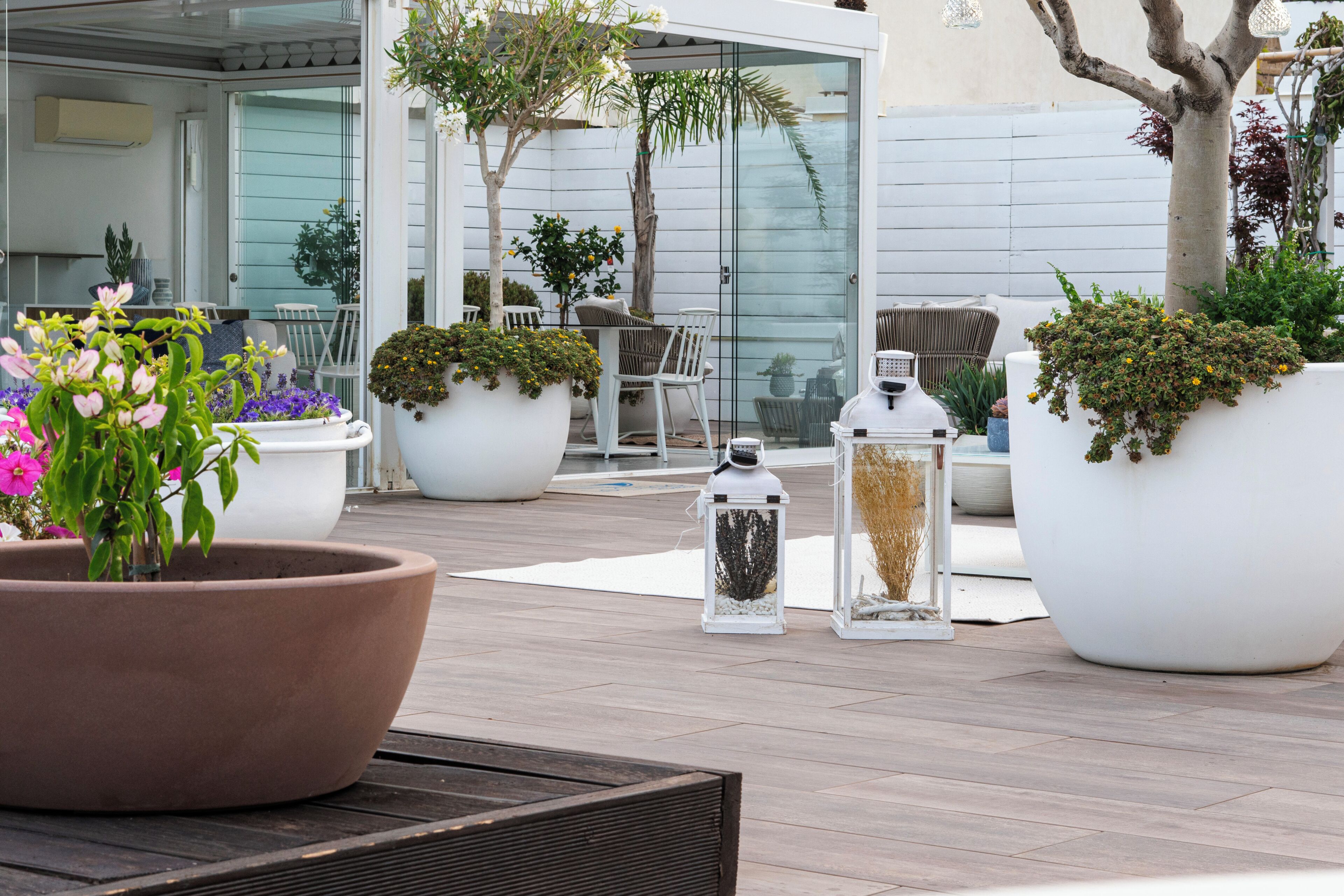 An outdoor patio area with large planters, a seating arrangement, and a glass door leading to a room.