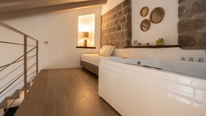 Ein modernes Badezimmer mit einer großen weißen Badewanne, Holzboden, Steinwand und einem kleinen Fenster mit einer Lampe.