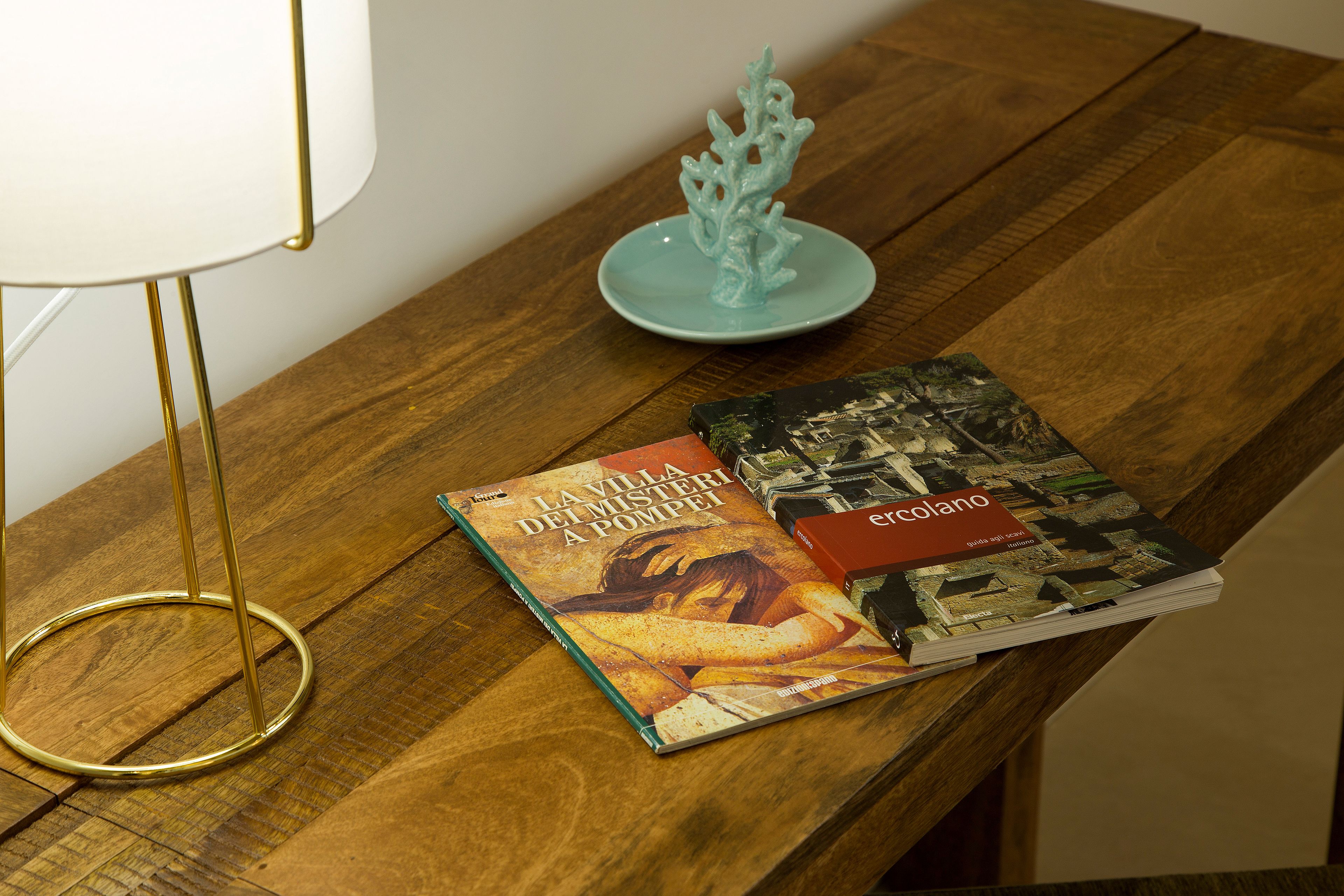 Een houten tafel met een lamp, een decoratief koraal en twee boeken.