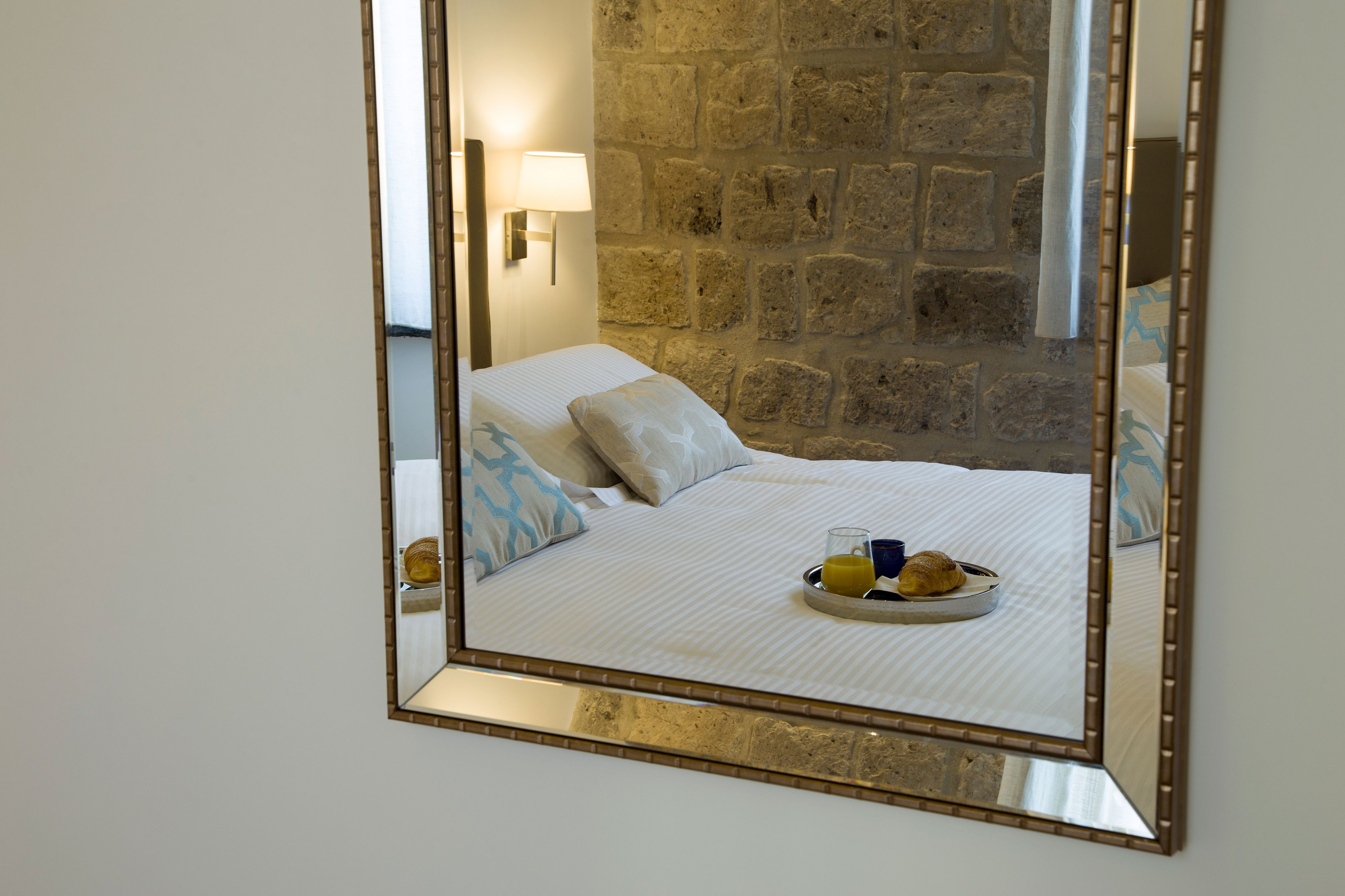 A bed with a tray of breakfast items, a lamp, and a stone wall.