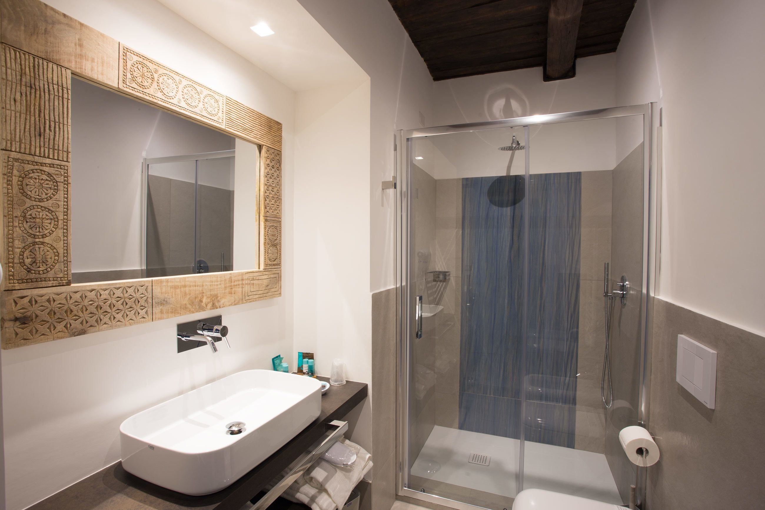 Ein modernes Badezimmer mit einem großen, weißen Waschbecken, einer in Glas eingefassten Dusche und einer Holzvertäfelung über dem Spiegel.