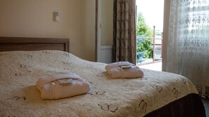 Habitación de hotel con cama, dos toallas, ventana con cortinas y vistas a zonas verdes.