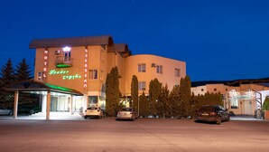 Un hotel con fachada curva, un acceso cubierto y varios coches aparcados en la entrada.