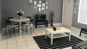 Un salon moderne avec une table à manger ronde, des chaises noires et blanches, un téléviseur à écran plat, une table basse et un tapis rayé noir et blanc.